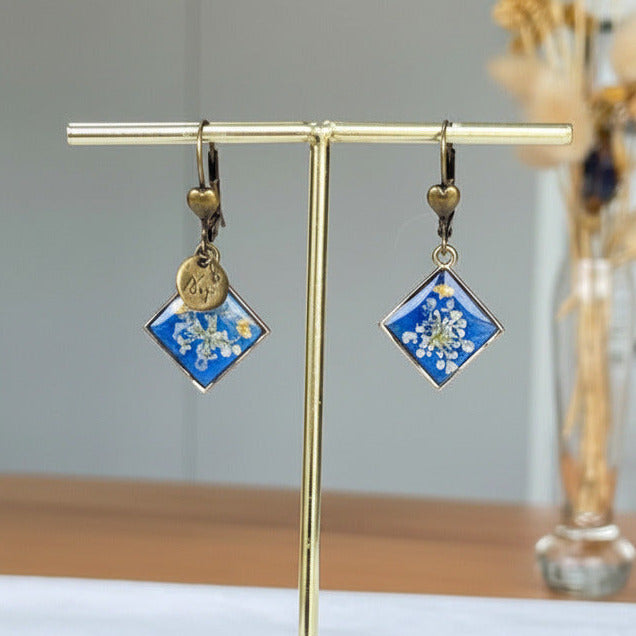Boucles d'oreilles bronze Sajecréa, fleurs de Carotte sauvage sur fond bleu électrique.