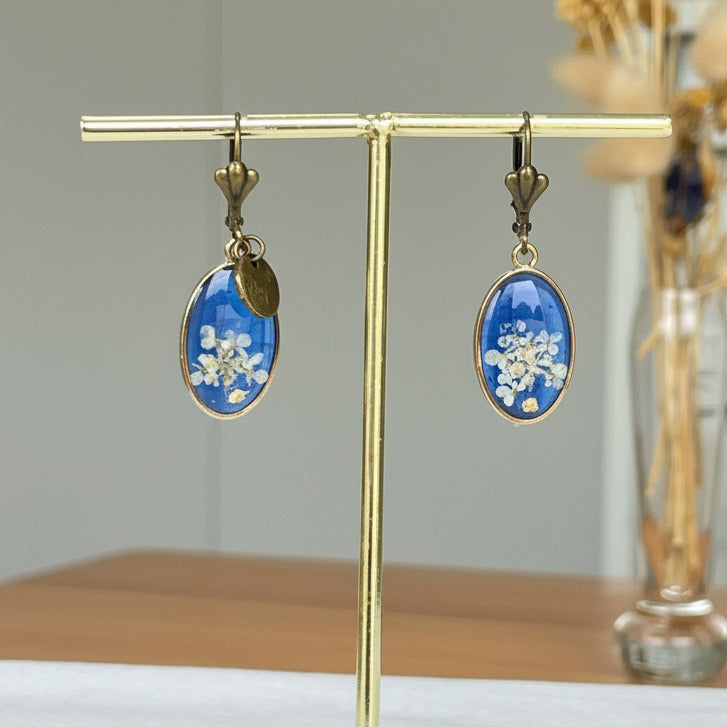 Boucles d'oreilles bronze Sajecréa, fleurs de Carotte sauvage sur fond bleu électrique.